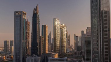 Dubai şehir merkezi ve finans bölgesinde caddelerde trafiği olan fütürist kuleler ve gökdelenler. Şehir silueti, gün doğumunda havadan sabah saatleri. Sıcak ışık ve güneş camdan yansıyor.