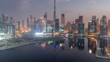 Dubai Business Bay ve Downtown 'ın havadan görüntüsü. Kanal boyunca çeşitli gökdelenler ve kuleler var. Gece gündüz geçiş zamanları. Güneş doğmadan önce vinçleri olan inşaat alanı