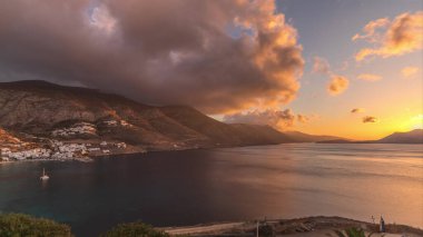 Panorama, Amorgos adasında gün batımında turuncu bulutları gösteriyor. Geleneksel Yunanistan - tepelerde beyaz evler ve turkuaz deniz, Kiklad