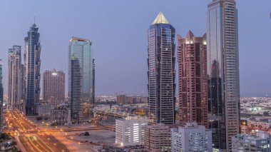 Business Bay semtinin ufuk çizgisi gece gündüz modern mimari geçiş zamanı yukarıdan. Güneş doğmadan önce Dubai gökdelenlerinin ve ana karayolu yakınlarındaki kulelerin havadan görüntüsü. Yol ayrımında trafik