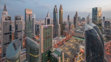 Sheikh Zayed Yolu 'ndaki yüksek binaların gökyüzü manzarası gece gündüz Dubai hava geçiş zamanı, BAE. Uluslararası Finans Merkezi 'ndeki gökdelenler güneş doğarken uzun gölgelerle tepeden görünüyor.