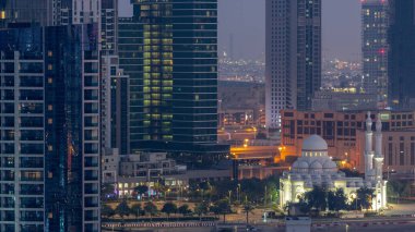 Bay Bulvarı yakınlarındaki yeni beyaz cami. Alışveriş merkezi Business Bay hava sahasında gökdelenlerle çevrili. Gün doğumundan önce geçiş zamanı. Otoparkın yanındaki yolda trafik vardı.