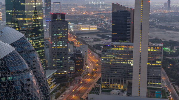 Skyline view of the high-rise buildings on curved road in Dubai aerial night to day transition timelapse, UAE. Office skyscrapers in International Financial Centre from above before sunrise