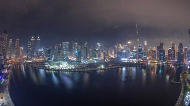 Dubai Business Bay ve Downtown 'ın gökdelenleri ve kuleleri kanal boyunca gece zaman çizelgesinde yer alan gökyüzü manzarası. Vinçli inşaat alanı