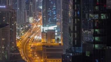 Tüm gece boyunca Dubai 'deki yoğun yol kavşağına yukarıdan hava görüntüsü. Arabalar iki yöne de doğru ilerliyor. Yüksek kuleleri olan iş sahası bölgesi