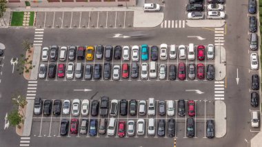 Otoparka park etmiş bir sürü renkli arabanın hava manzarası. Gün boyunca yer ve yönler için çizgiler ve işaretler var. Uzun gölgeler hızlı hareket ediyor. Dubai finans bölgesi bulvarı