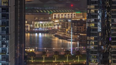 Şehir merkezindeki Dubai Çeşmesi 'nin havadan görünüşü, alışveriş merkezinin yanında palmiyeler ve bayraklar ve UAE' deki gece ve gündüz geçiş zamanının yanında. Gün batımından sonra iki gökdelen arasında görüldü.