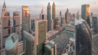 Sheikh Zayed Yolu 'ndaki yüksek binaların gökyüzü manzarası gece gündüz Dubai hava geçiş zamanı, BAE. Uluslararası Finans Merkezi 'ndeki gökdelenler güneş doğarken uzun gölgelerle tepeden görünüyor.