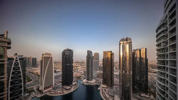 Sunrise over tall residential buildings at JLT district aerial timelapse during all day, part of the Dubai multi commodities center mixed-use district. Skyscrapers around pond with shadows moving fast