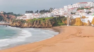 Geniş kumlu sahil ve Albufeira zamanındaki Atlantik Okyanusu. Uçurumun tepesindeki beyaz evler. Asansör perspektiften sahile doğru. Yukarıdan hava görüntüsü. Algarve, Portekiz