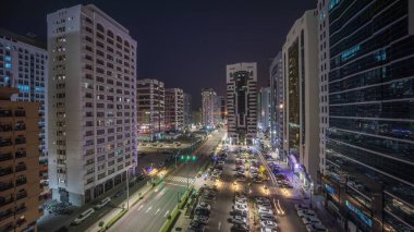 İkamet binaları ve Abu Dabi hava saatinin modern şehir mimarisi tüm gece boyunca gün doğumuna kadar, BAE. Otoparkta yukarıdan arabalara ve gökdelenli kulelerin uzun gölgelerine bak