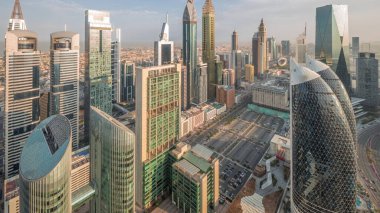 Sheikh Zayed Yolu 'ndaki yüksek binaların gökyüzü manzarası gece gündüz Dubai hava geçiş zamanı, BAE. Uluslararası Finans Merkezi 'ndeki gökdelenler güneş doğarken uzun gölgelerle tepeden görünüyor.