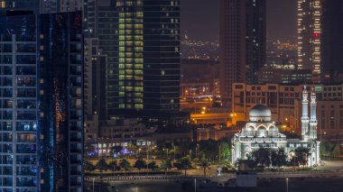 Bay Bulvarı yakınlarındaki yeni beyaz cami. Alışveriş merkezi, Business Bay hava sahasındaki aydınlık gökdelenlerle çevrili. Tüm gece boyunca. Otoparkın yanındaki yolda trafik vardı.
