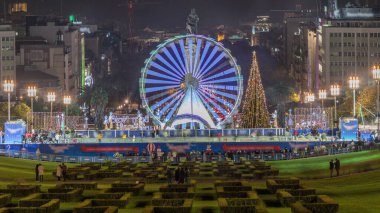 Portekiz 'in Lizbon şehrindeki geleneksel Eduardo VII parkında düzenlenen Noel etkinliğinde dönme dolap. İnsanlar Noel ağacının yanında buz pateni yapıyor. Yukarıdan görüntüle