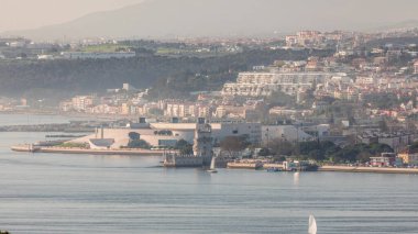 Portekiz 'in Lizbon şehrinin en ünlü simgelerinden biri olan Belem Kulesi zaman çizelgesinin hava görüntüsü. Gün batımından önce sisli hava. Rıhtımda yürüyen insanlar ve arka planda binalar