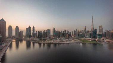 Dubai Business Bay ve Downtown 'ın havadan manzarası kanal boyunca çeşitli gökdelenler ve kuleler ile gündüz ve gece geçiş zamanı. Gün batımından sonra vinçleri olan inşaat alanı