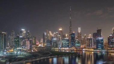 Panorama, Dubai Business Bay ve Downtown 'ın kanal gece zaman çizelgesi boyunca çeşitli gökdelenleri ve kuleleri ile hava manzarasını gösteriyor. Vinçli inşaat alanı