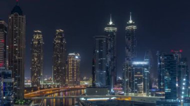 Dubai Business Bay 'in aydınlık gökdelenleri ve tüm gece boyunca su kanalı antenleri olan şehir manzarası. Rıhtımda konut ve ofis kuleleri olan modern gökyüzü. Ay batıyor