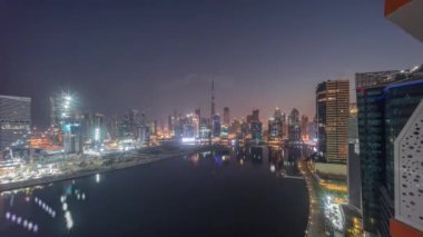 Dubai Business Bay ve Downtown 'ın çeşitli gökdelenleri ve kuleleri ile hava manzarası kanal boyunca gece gündüz geçiş zamanı. Güneş doğmadan önce vinçleri olan inşaat alanı