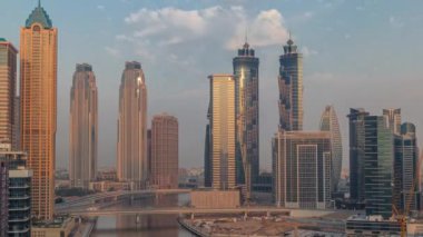 Dubai İşletme Koyu 'nun gökdelenleri ve su kanalı sabah saatleri ile şehir manzarası. Gündoğumunda konut ve ofis kuleleri olan modern gökyüzü. Güneş cam yüzeyden yansıyor