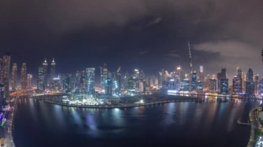 Dubai Business Bay ve Downtown 'ın gökdelenleri ve kuleleri kanal boyunca gece zaman çizelgesinde yer alan gökyüzü manzarası. Vinçli inşaat alanı