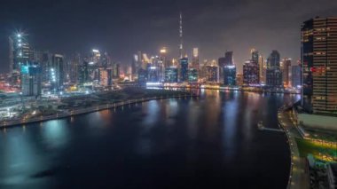 Dubai Business Bay ve Downtown 'a giden hava panoramik bir manzara. Gece boyunca kanal boyunca çeşitli gökdelenler ve kuleler var. Vinçleri olan bir inşaat alanı. Yanıp sönen ışıklar