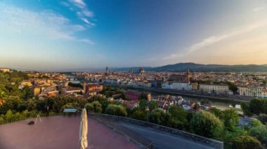 Floransa şehrinin gündoğumundaki panoramik zaman çizelgesinin en üst görüntüsü. Arno nehir köprüleri ve tarihi binalar, arka planda dağlar. Yeşil ağaçlar, yaz gününde mavi bulutlu gökyüzü