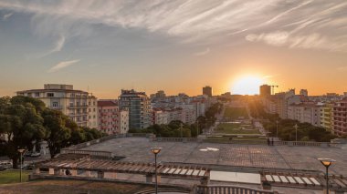 Panorama Alameda Dom Afonso Henriques 'deki çimlerin üzerinde gün batımını renkli binalar ve Aydınlık Çeşme hava saatleriyle gösteriyor. Lizbon, Portekiz 'de akşam gökyüzü ile yukarıdan görünüm