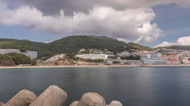 Panorama showing view of Sesimbra Town and Port timelapse, Portugal. Skyline landscape with boats, houses and beach from lighthouse on a pier. Resort in Setubal district clipart