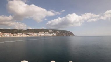 Panorama, Portekiz 'deki Sesimbra Town ve Port Timelapse manzarasını gösteriyor. İskeledeki deniz fenerinden kayıklar, evler ve plajlarla dolu bir gökyüzü manzarası. Setubal bölgesinde bir tatil köyü. Güzel bulutlar