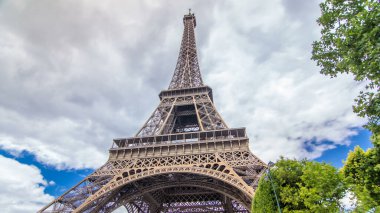 Champ de Mars ve Eyfel Kulesi güneşli bir yaz gününde hızlandırılmış zaman atlaması. Paris, Fransa. Yeşil ağaçlar ve bulutlu gökyüzü. Geri çekiliyorum