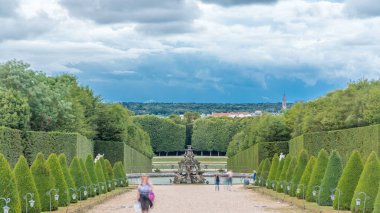 Bahçede bakımlı bir sokak ve yukarıdan gelen zaman aralığında çeşme. Versailles Şatosu 'nda (Chateau de Versailles) güzel bir bahçe, Fransa. Yaz gününde dramatik bulutlu gökyüzü
