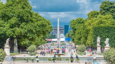 Tuileries Sarayı 'nda yürüyen insanlar açık hava parkı zaman dilimi. Arka planda kalabalık olan Champs Elysees ve Arc de Triomphe 'ye bakın. Bulutlu mavi gökyüzü ile yaz günü sahnesi. Paris, Fransa