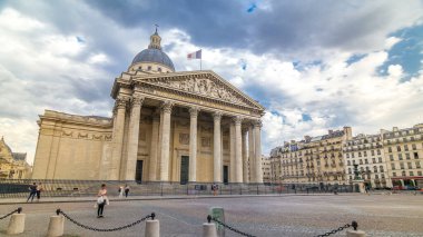 Ulusal panteon binası zaman atlaması, sokak manzarası ve yürüyen insanlar. Sokakta trafik, yaz gününde bulutlu hava. Üstte bayrak var. Paris, Fransa