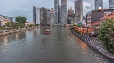 Singapur rıhtımı merkezi iş bölgesinde uzun gökdelenler ve Boat Quay 'de küçük restoranlar gün batımından sonra geçiş zamanı.