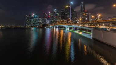 Esplanade Köprüsü ve şehir merkezindeki gökdelenler Singapur 'un arka planında gece gündüz geçiş zamanları. Aydınlatılmış kuleler suya yansıyor