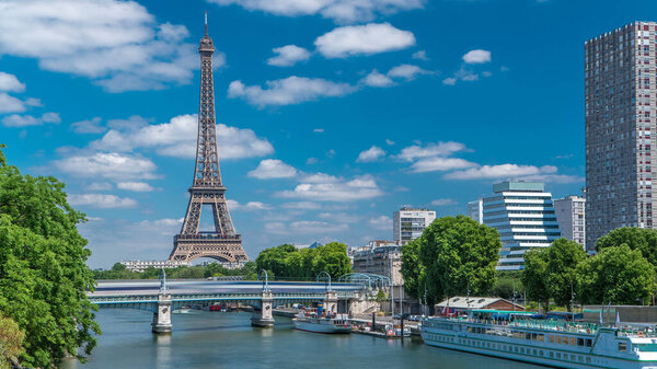 Eiffel tower at the river Seine timelapse from Grenelle bridge in Paris, France. Isle of the Swans and ship on river at sunny summer day under white clouds