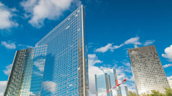 Glass mirror surface skyscraper timelapse in famous financial and business district of Paris - La Defense. Reflections on a glass with blue clouds and blue sky at summer day