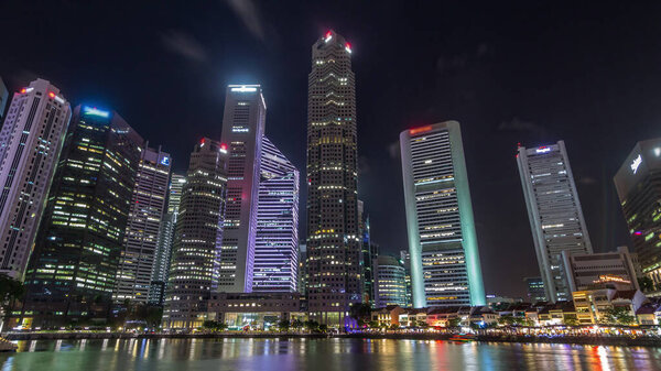 Singapore quay with tall skyscrapers in the central business district and small restaurants on Boat Quay night timelapse hyperlapse. Towers reflected in water
