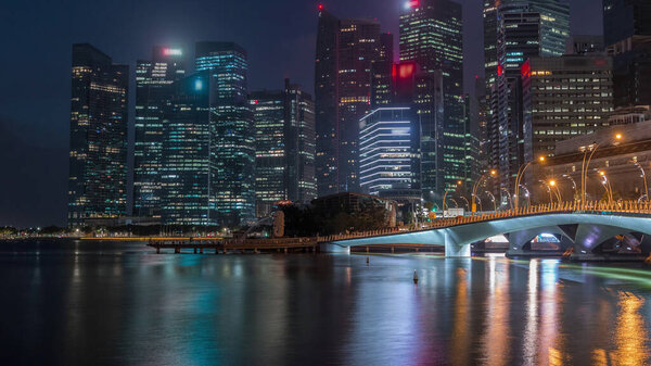 Esplanade bridge and downtown core skyscrapers in the background Singapore night to day transition timelapse. Illuminated towers reflected in water