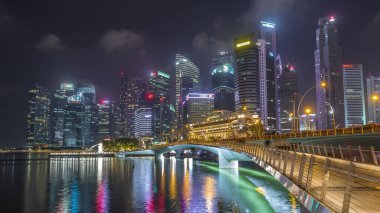 Esplanade Köprüsü ve şehir merkezindeki gökdelenler arka planda Singapur 'da gece vakti hızlandırılmış. Aydınlatılmış kuleler suya yansıyor