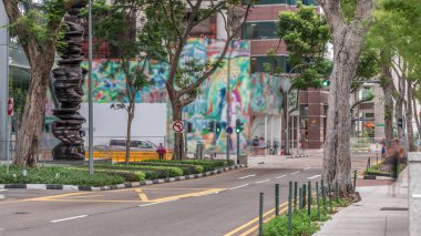 Battery Road Bulvarı 'nda trafik var ve Singapur' un şehir merkezinde yeşil ağaçlarla çevrili. Yeşil çimlerin yanında yürüyen insanlar