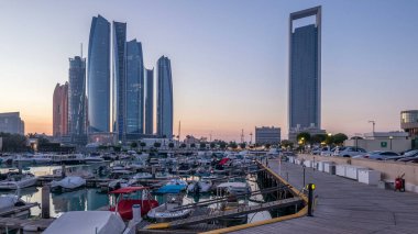 Al Bateen marinası Abu Dabi, gün batımından gün batımına kadar. Limanda tekneler ve arka planda aydınlatmalı modern gökdelenler.