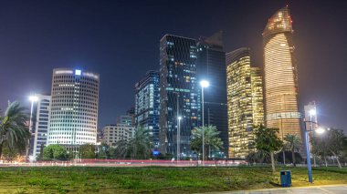 Abu Dabi 'deki gökdelenler gece gökdelenleri, Birleşik Arap Emirlikleri. Aydınlatılmış modern kuleleri ve caddelerde trafiği olan Corniche 'den görüntü