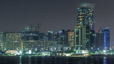 Abu Dabi Skyline 'ın panoramik görüntüsü ve gece vakti deniz manzarası, Birleşik Arap Emirlikleri. Aydınlatılmış gökdelenleri ve şantiyesi olan Corniche manzarası