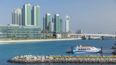 Abu Dabi 'deki Al Maryah Adası' nın modern binaları motorlu tekneler ve rıhtımla ufuk çizgisi zaman çizgisi. Sudaki gökdelenlerin yansımalarıyla köprüden görünüm