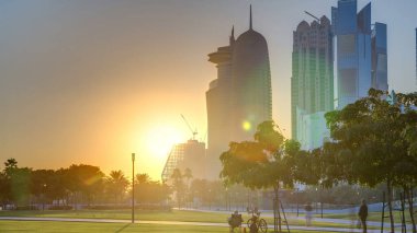 Gün batımında Doha 'nın yüksek katlı zaman diliminde, Hotel Park' tan yeşil çimenli ve ön planda suni tepe ile görüldü. Gökdelenler ve palmiyeler