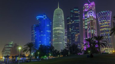 Doha 'nın yüksek katlı bölgesinde gece vardiyası, parktan görülmüş. Batı körfezinde aydınlatılmış gökdelenler ve palmiyeler