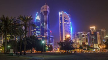 Doha 'nın yüksek katlı bölgesinde gece vardiyası, parktan görülmüş. Batı körfezinde aydınlatılmış gökdelenler ve palmiyeler