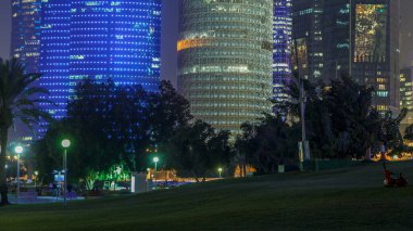Doha 'nın yüksek katlı bölgesinde gece vardiyası, parktan görülmüş. Batı körfezinde aydınlatılmış gökdelenler ve palmiyeler